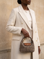 Model in an ivory coat holding the Houndstooth Deauville in hand by a limestone wall
